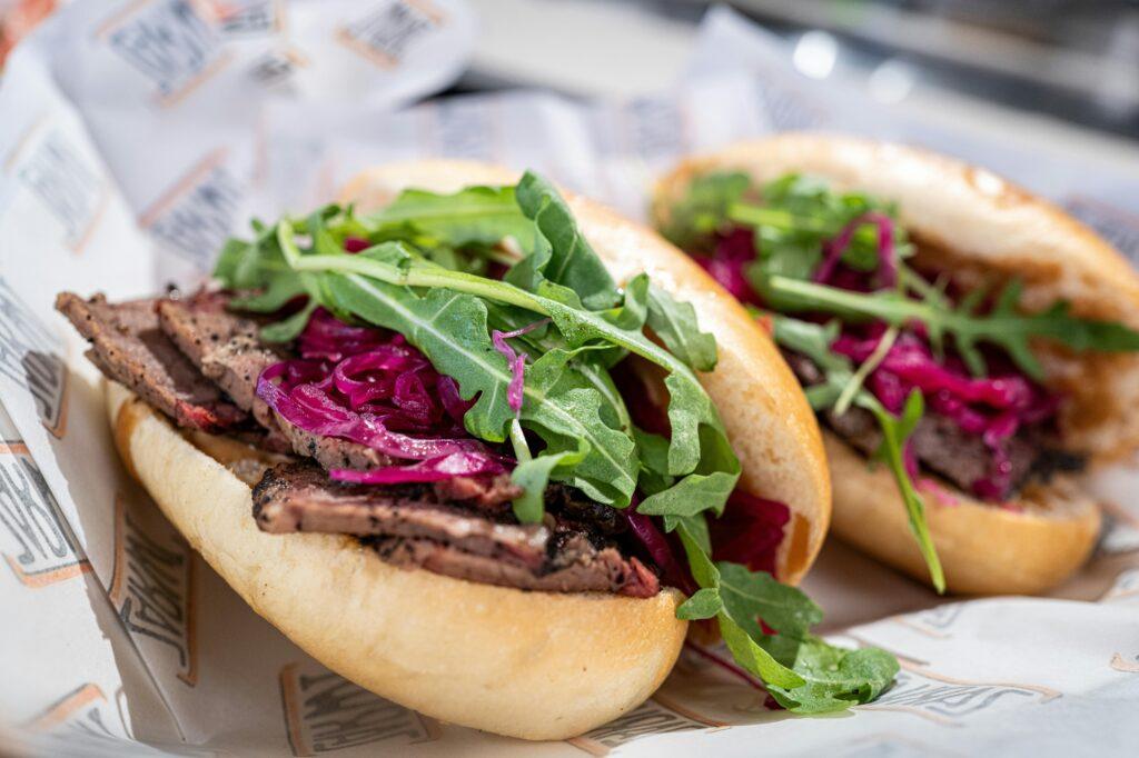 Close-up of a tasty pastrami sandwich with fresh arugula, pickles, and a soft bun.