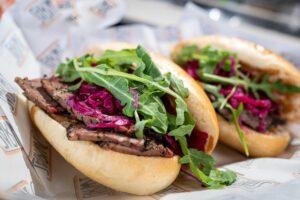 Close-up of a tasty pastrami sandwich with fresh arugula, pickles, and a soft bun.