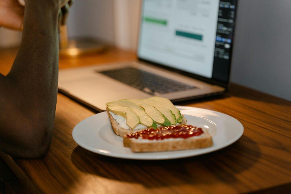 A workspace setup with avocado toast next to a laptop, perfect for remote work inspiration.